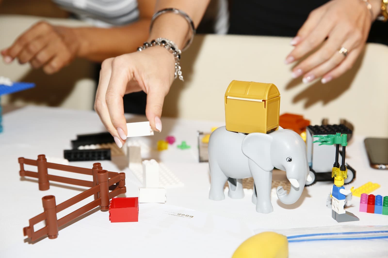 Hands reaching for bricks beside a LEGO elephant carrying a treasure chest