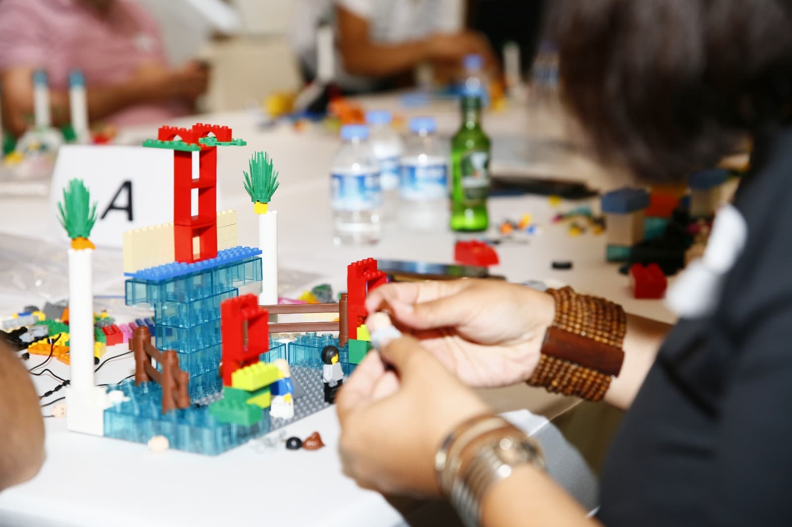 Hands building a translucent blue tower model at a workshop table