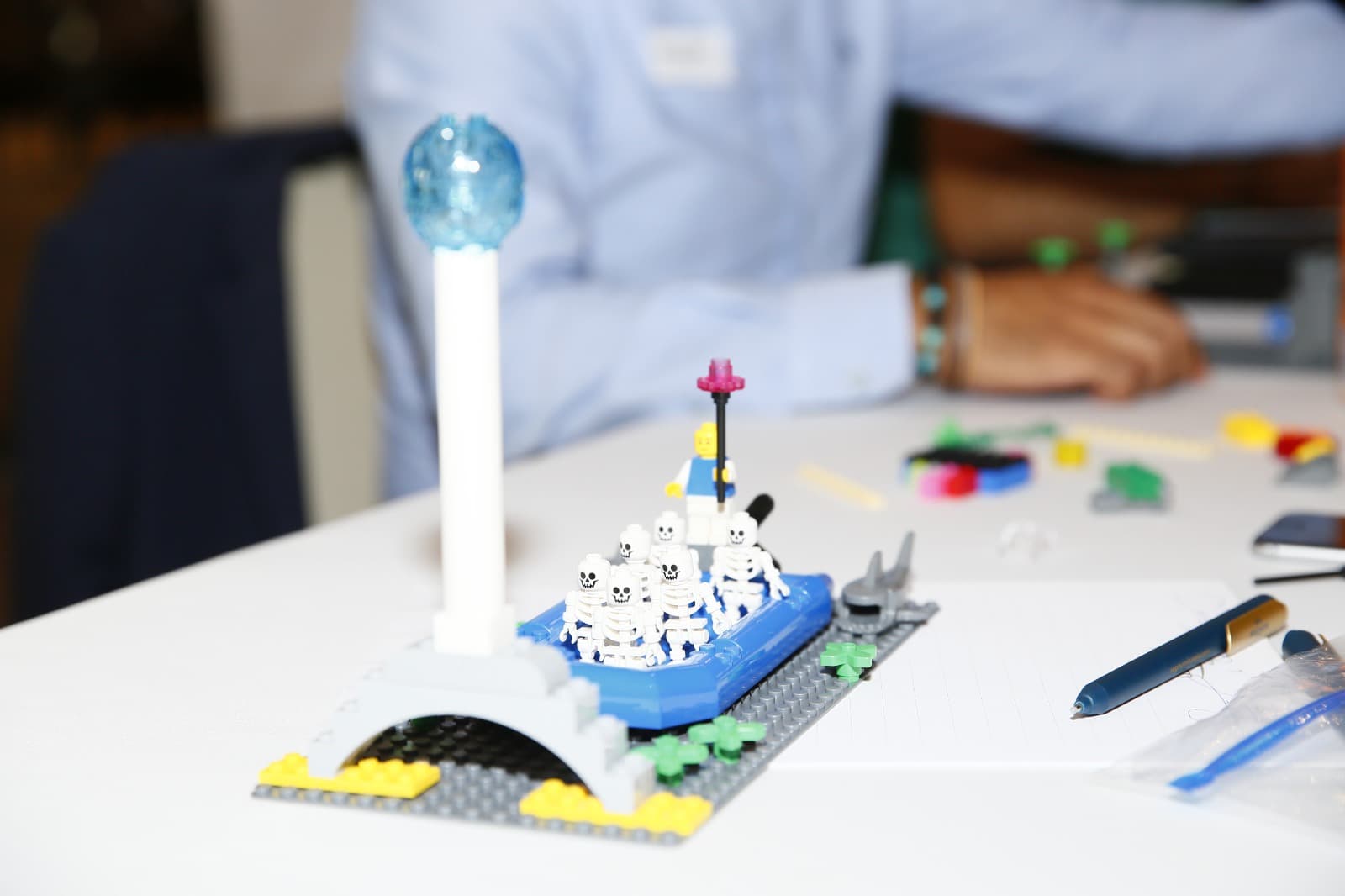 A LEGO model of a boat carrying skeleton figures past a lighthouse